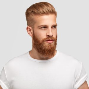 Serious thoughtful male with ginger beard, dressed casually, focused somewhere, isolated over white background with free space on right for your advertising content. Pensive red haired hipster